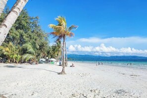 Une plage de sable blanc, bordée de palmiers, sous un ciel bleu azur.