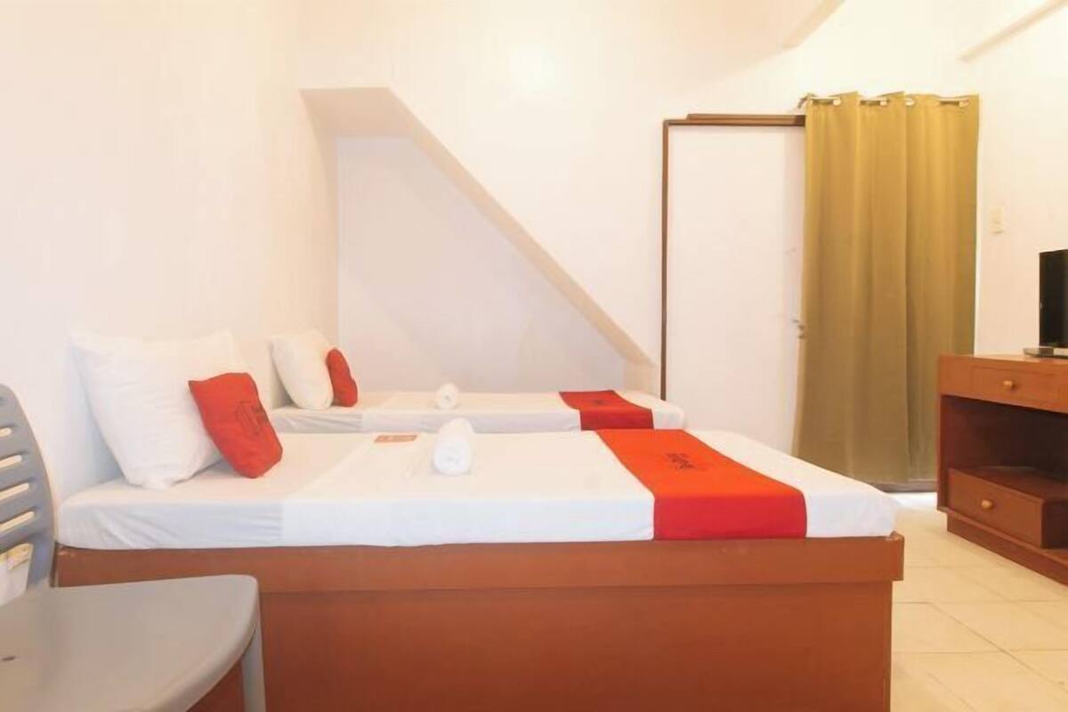 A hotel room with two beds, a desk, a chair, a TV, and a window with curtains.