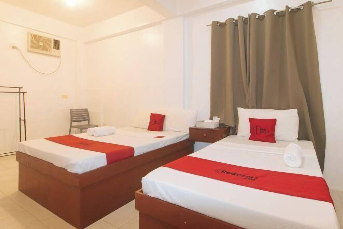 A hotel room with two beds, a chair, a small table, and a window with curtains.