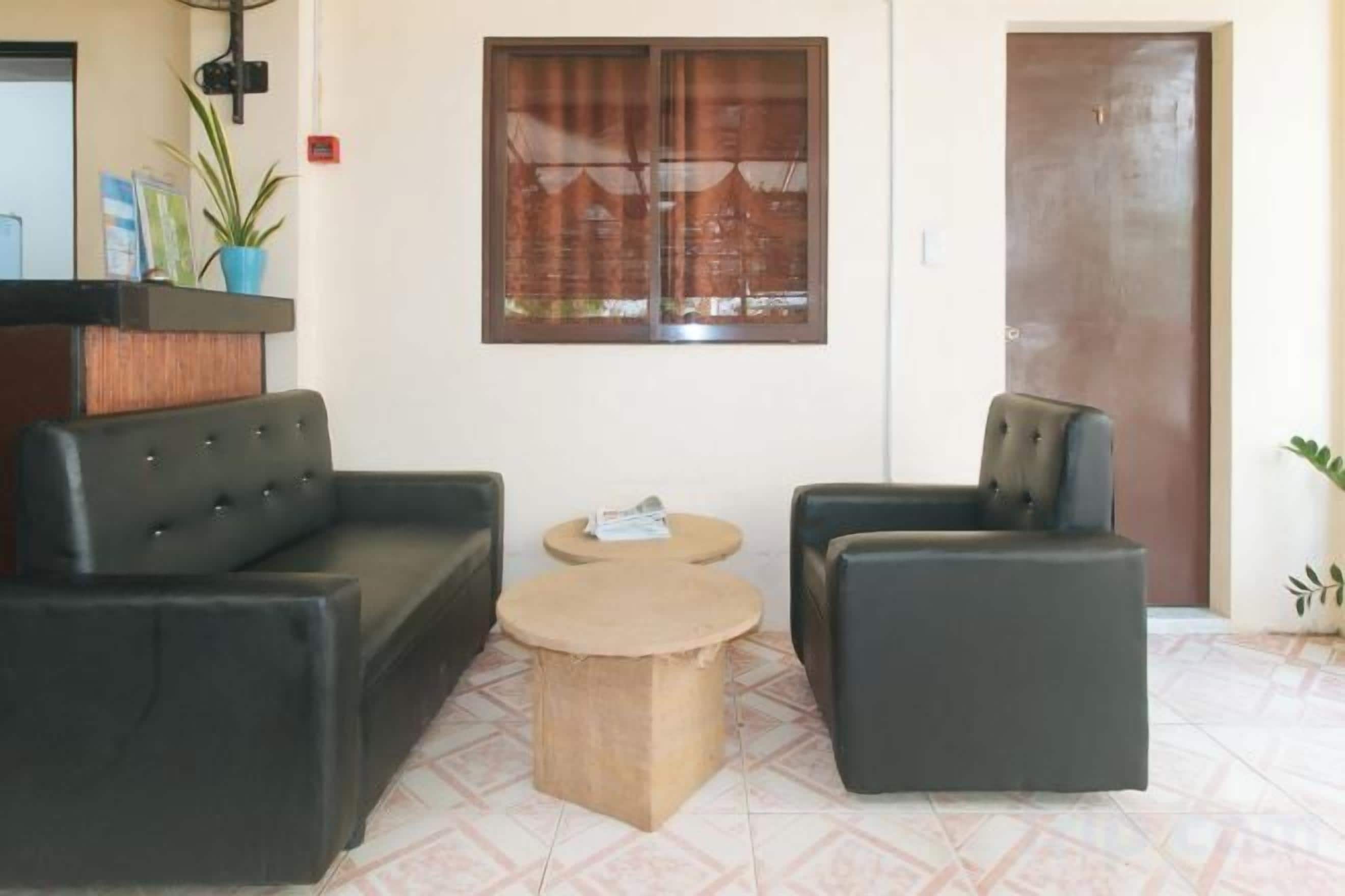 A reception area with a reception desk, two black sofas, a round coffee table, and a window with blinds.