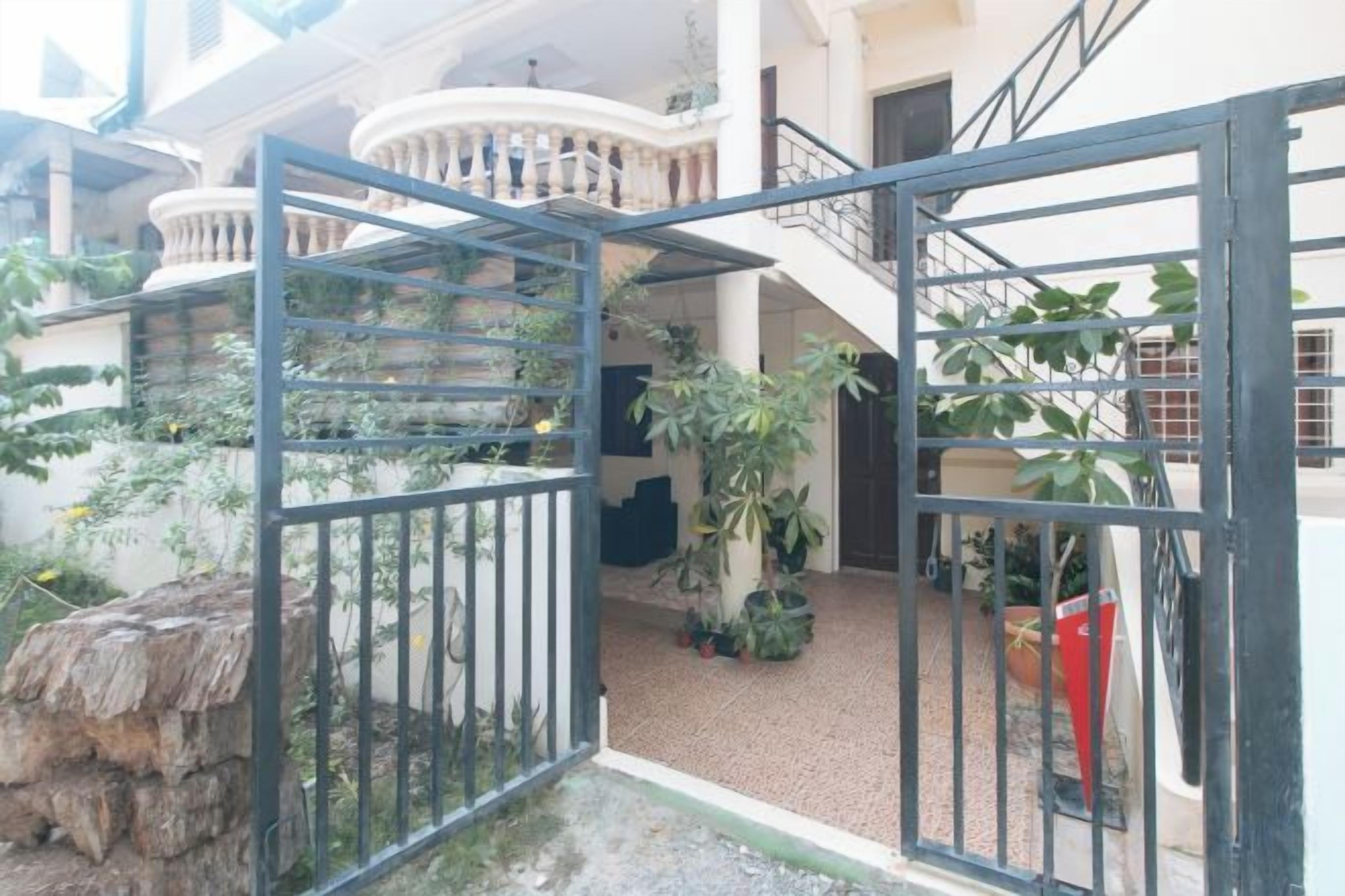 A gated courtyard with a staircase leading to a balcony, surrounded by potted plants and a stone wall.