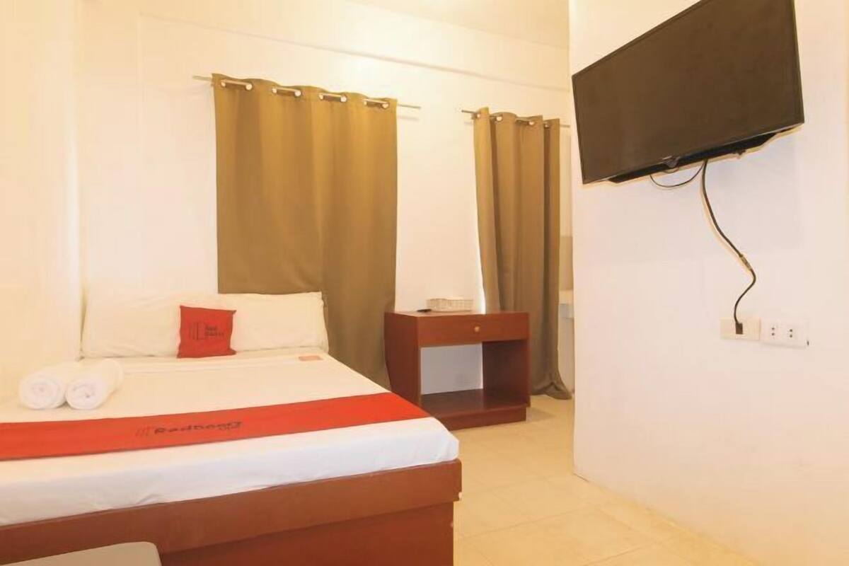 A hotel room with a bed, a nightstand, a TV mounted on the wall, and curtains.
