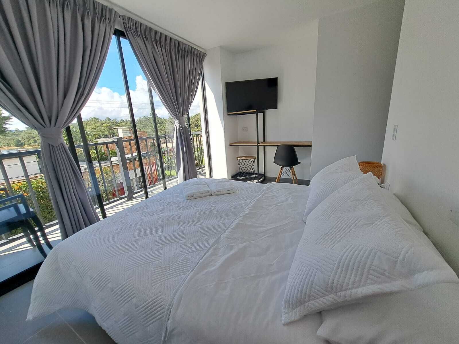 Quarto de hotel com cama grande, televisão de tela plana e varanda com cortinas.