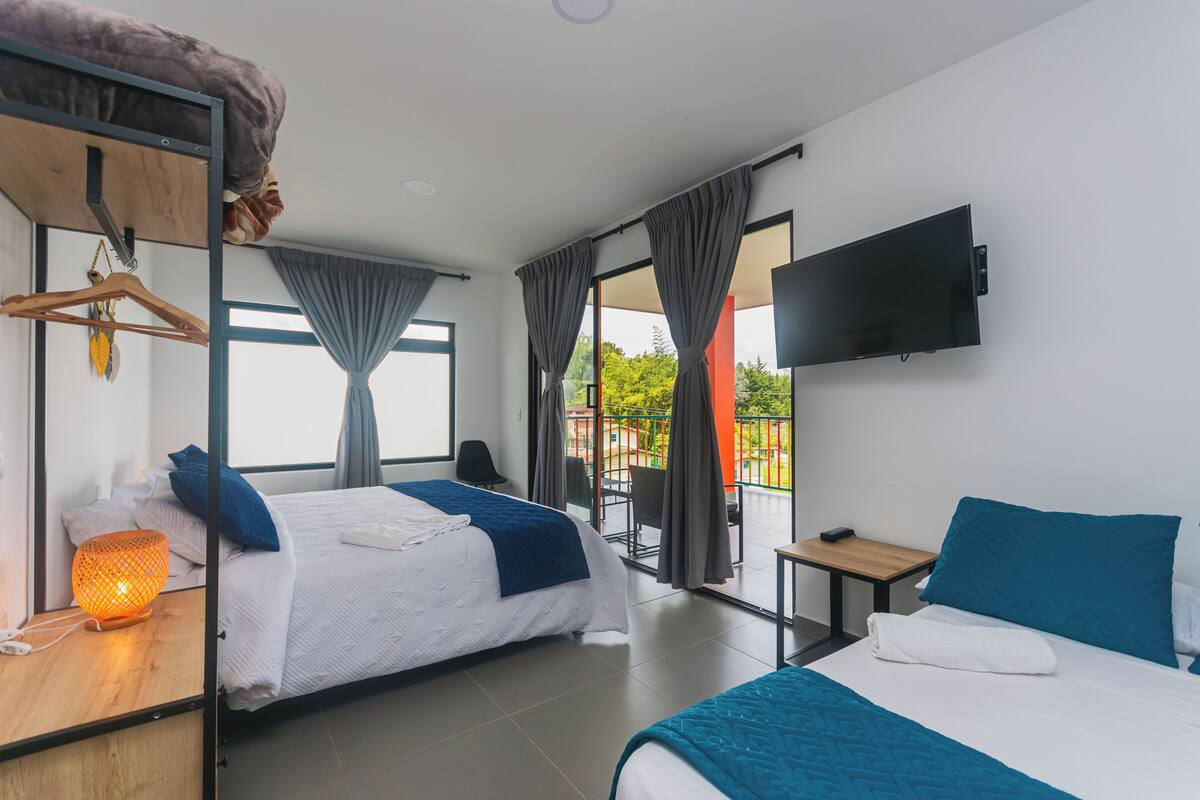 A hotel room with two beds, a TV, a balcony, and a wooden desk.