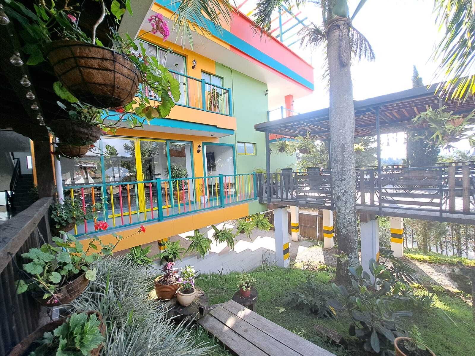 Un bâtiment coloré à deux étages, doté de balcons et entouré d’une végétation luxuriante et de plantes en pot.