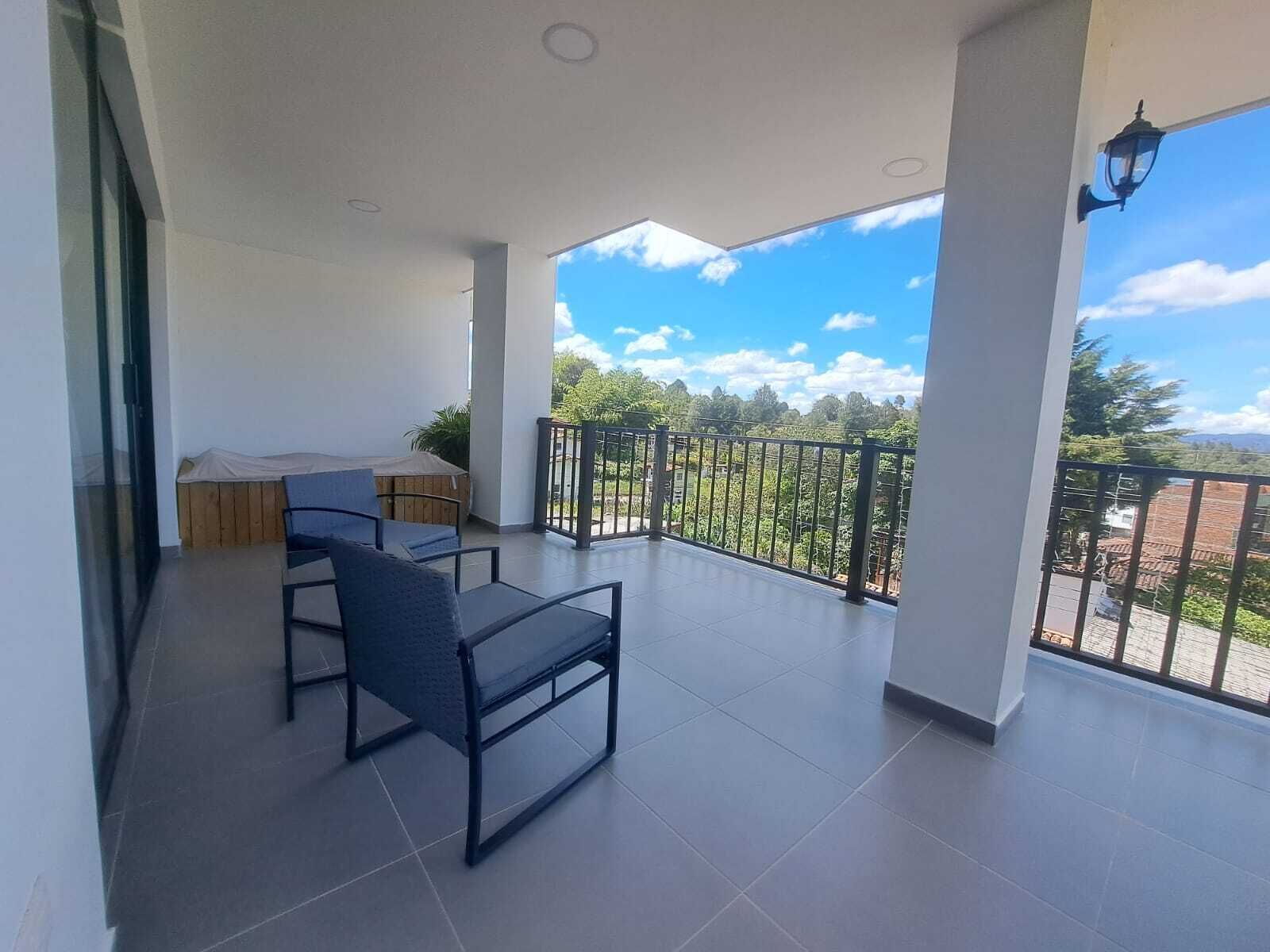 A balcony with a view of greenery and mountains, a covered seating area, and a tiled floor.
