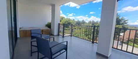 A balcony with a view of greenery and mountains, a covered seating area, and a tiled floor.