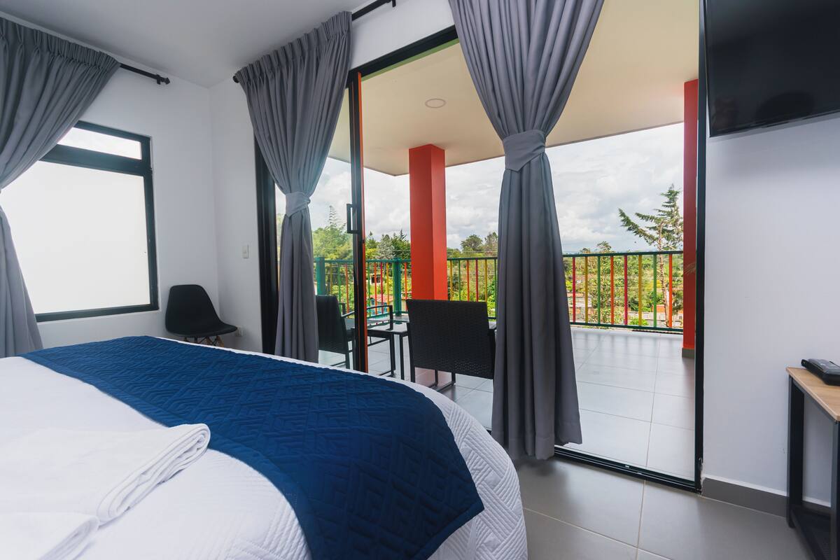 A hotel room with a large bed, a balcony with a view, and a TV on the wall.