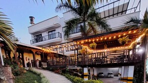 A courtyard with a covered outdoor seating area, a pathway leading to a building, and a parking area. - Country House Hotel (Guatapé)