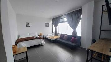 A modern room with a bed, a sofa, a dining table, and a large window with curtains.