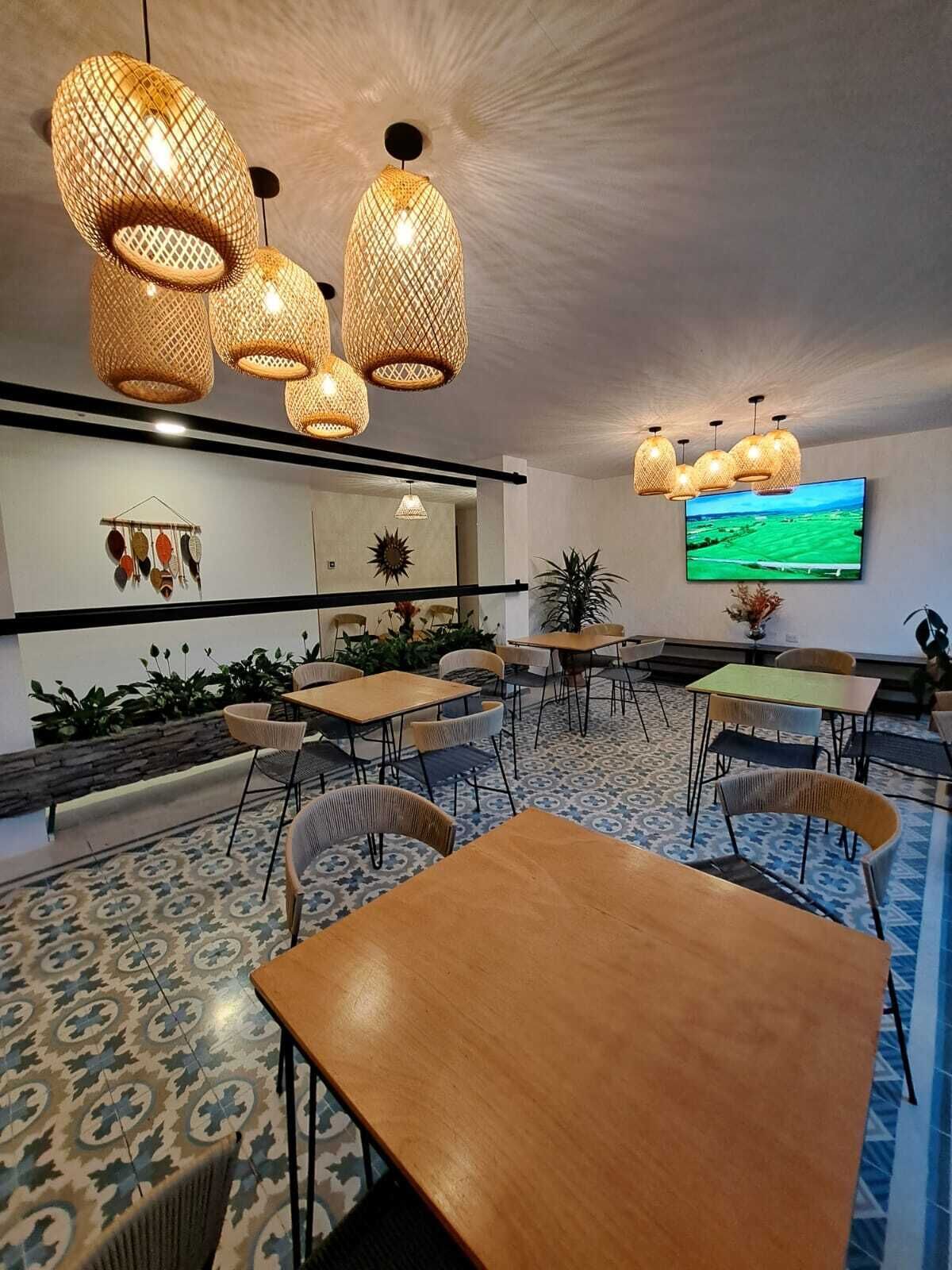 A modern dining area with wooden tables and chairs, woven pendant lights, a flat-screen TV, and decorative wall art.