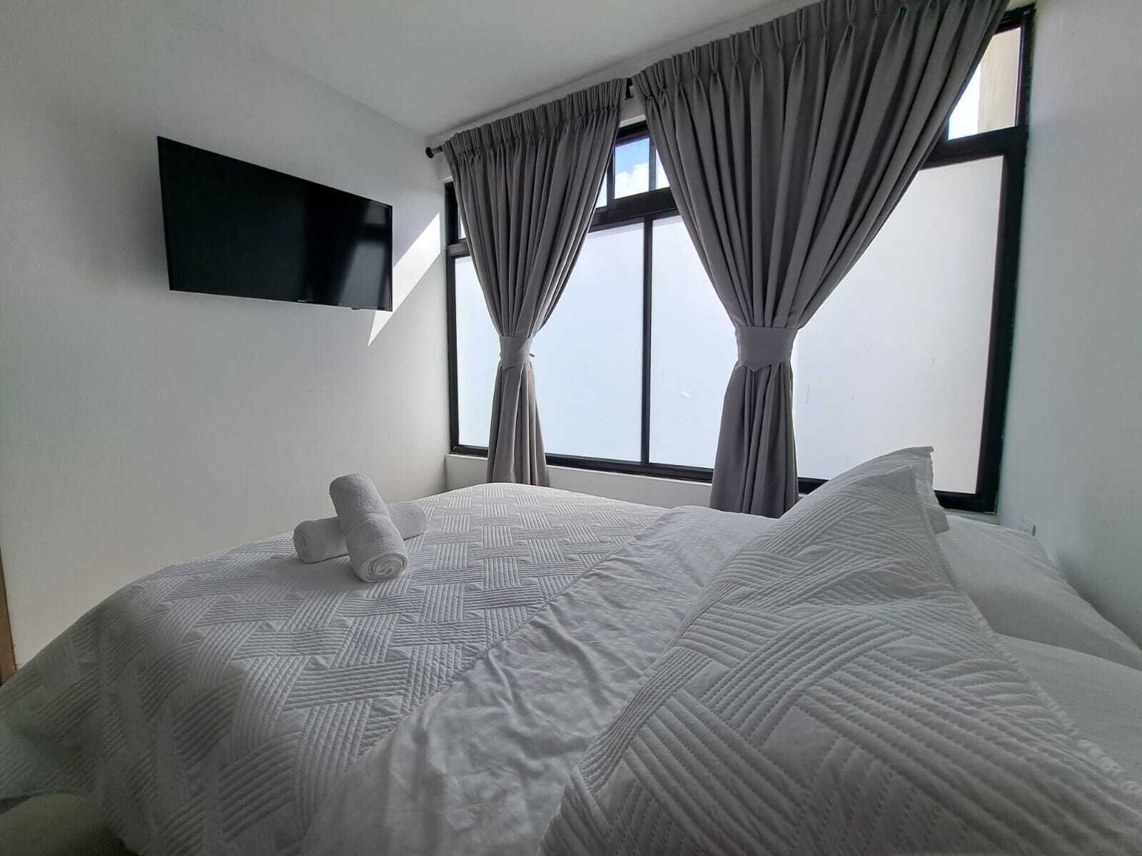 Habitación de hotel con cama, televisión de pantalla plana en la pared y ventana con cortinas.