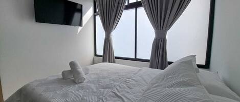 Habitación de hotel con cama, televisión de pantalla plana en la pared y ventana con cortinas.