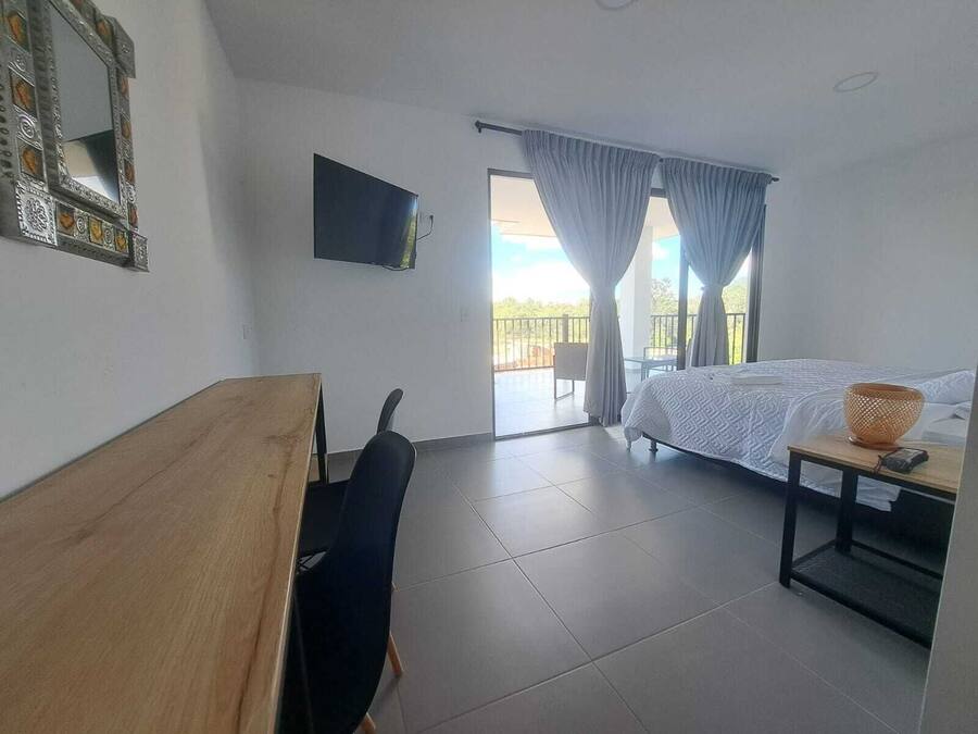 A hotel room with a bed, a desk, a chair, a television, and a balcony with curtains.