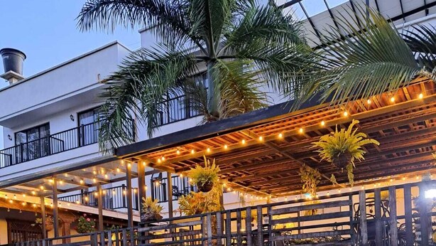 A covered outdoor area with seating, palm trees, and a parking garage in the background. - Country House Hotel (Guatapé)