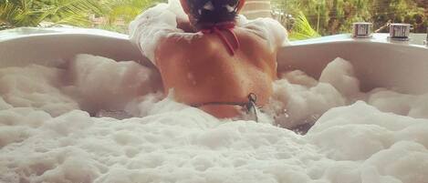 A person relaxing in a hot tub filled with bubbles, surrounded by greenery.