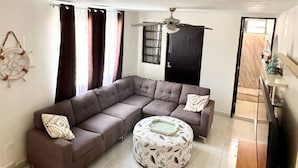 A living room with a sectional sofa, a round ottoman, a ceiling fan, and a view of the adjacent room. - Spacious 5-bedroom house in gated community, private pool and semi-private beach (Humacao)