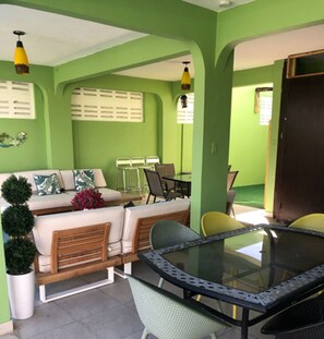 Une pièce décorée dans les tons de vert, avec une table à plateau de verre, des chaises, un canapé et une petite plante en pot.