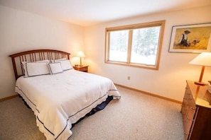 A bedroom with a bed, bedside lamps, a window, and a painting on the wall.