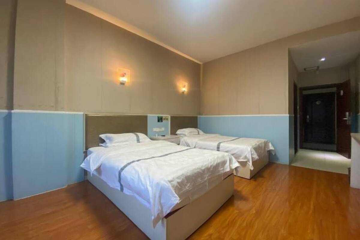 A hotel room with two beds, wooden flooring, and wall-mounted light fixtures.