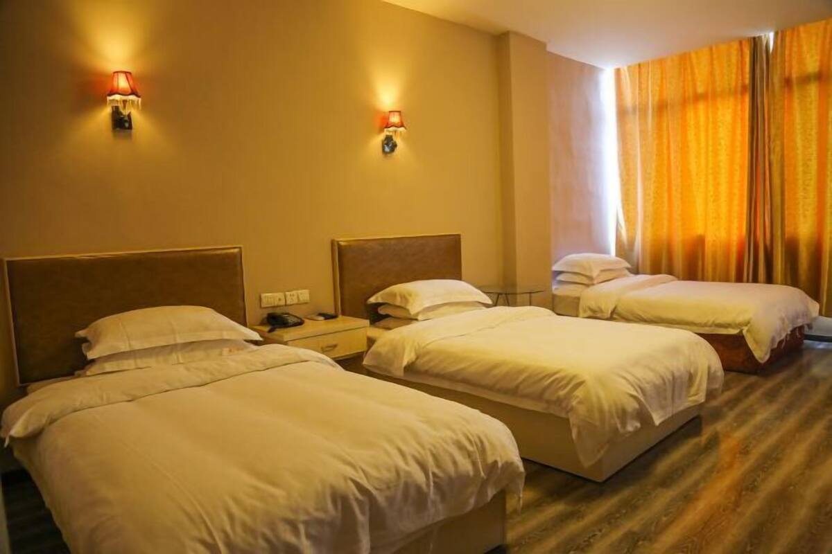 A hotel room with two single beds, a wooden headboard, a nightstand with a phone, and a window with curtains.