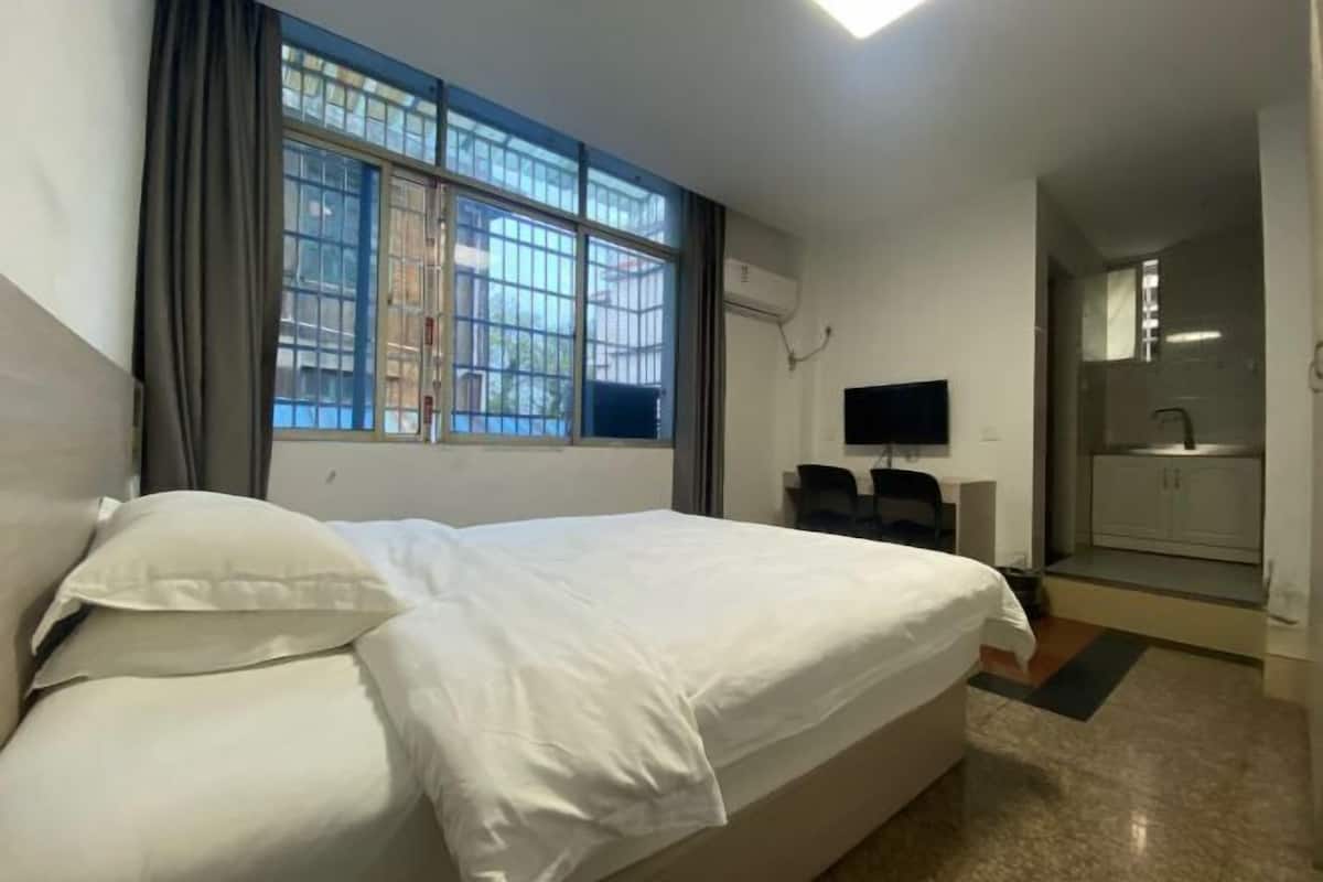 A hotel room with a bed, a TV, a small desk, and a bathroom visible through an open door.