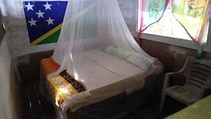 A small room with a bed under a mosquito net, a chair, and a flag on the wall. - Kajoro Sunset Lodge  (Vangunu Island)