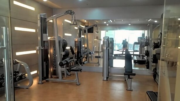 A gym with various exercise machines, a mirrored wall, and a wooden floor. - Palm Tree Genlex Condo (Pasay)