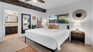 A bedroom with a large bed, a ceiling fan, a window with a view, a bedside table with a lamp, and a mirror. - Mountain views! Big private yard with pool - heat optional with fee & spa! (Tucson)