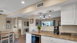 A modern kitchen with white cabinetry, granite countertops, and a built-in dishwasher. There is a coffee maker on the counter and a potted plant. - Mountain views! Big private yard with pool - heat optional with fee & spa! (Tucson)