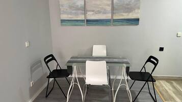 Uma sala de jantar com mesa de vidro e cadeiras, parede cinza e três quadros sobre a mesa.