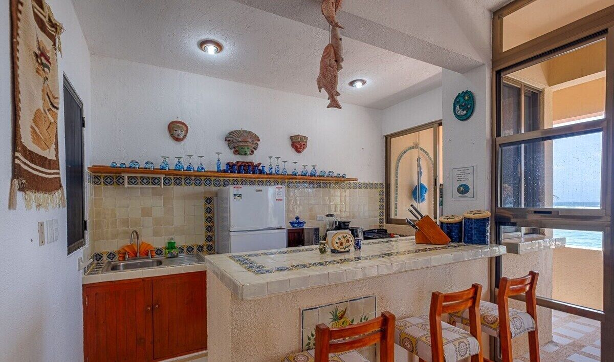 A kitchen with a tiled backsplash, wooden cabinets, and a bar area with chairs.