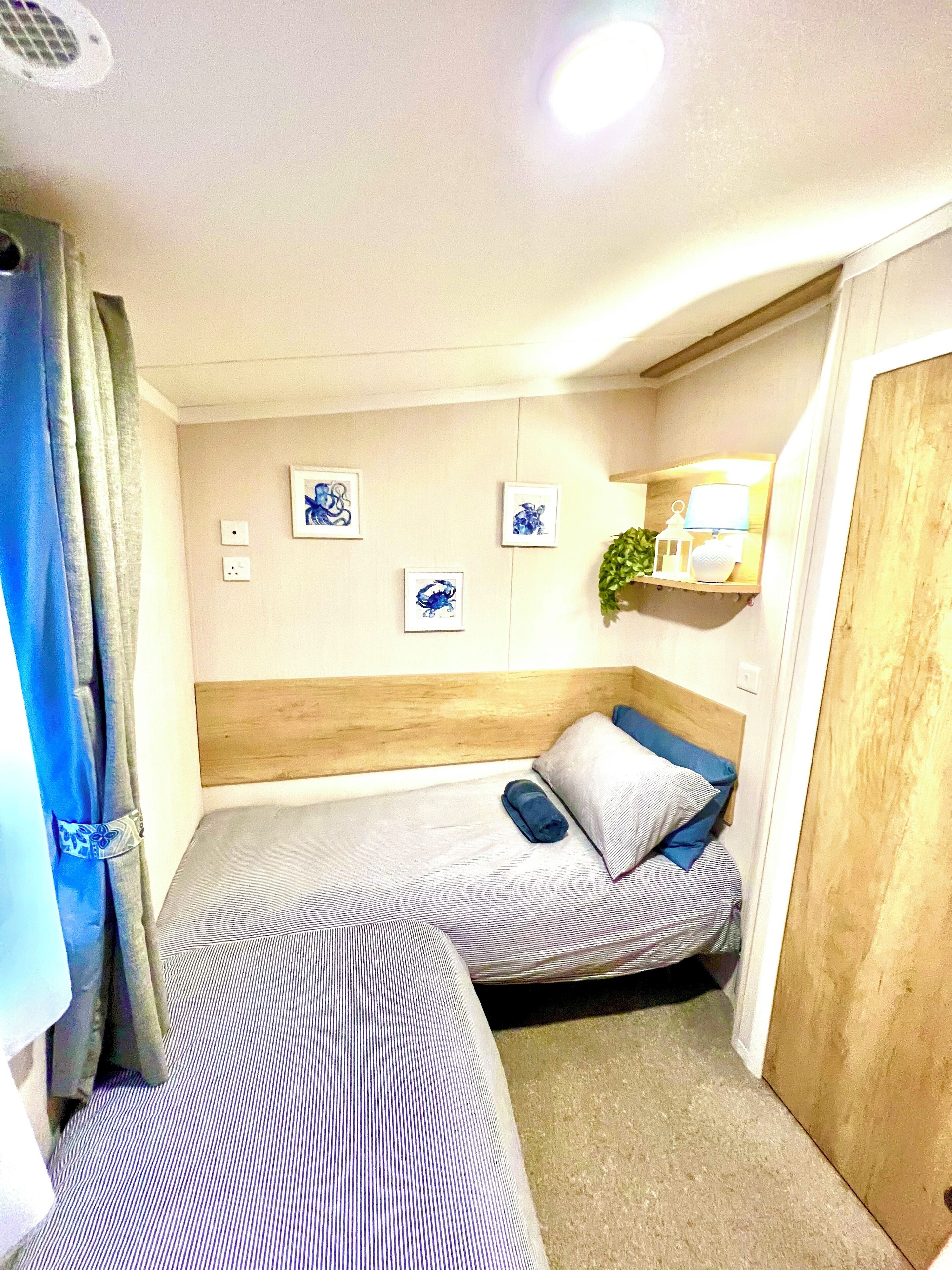A compact room with two beds, a small shelf with a plant, and a wall-mounted light fixture.