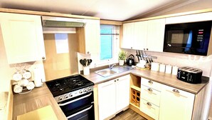 Een compacte keuken met een fornuis, oven, magnetron, spoelbak en houten keukenkastjes.