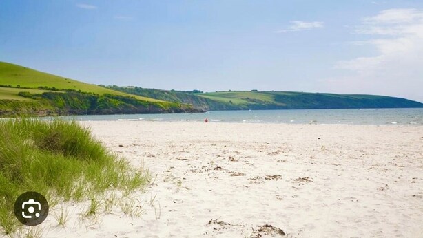 Een strand met wit zand, groen gras en een heldere lucht.
