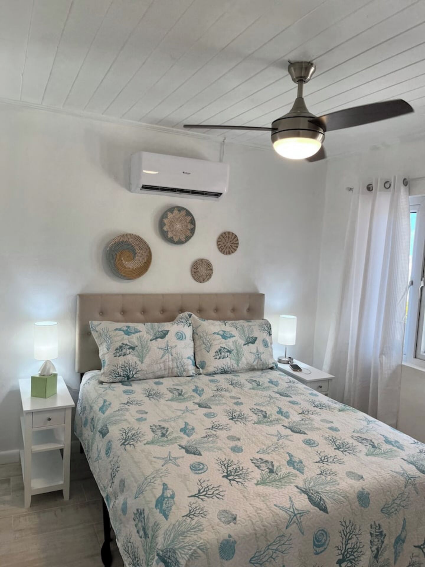 A bedroom with a bed, nightstands, an air conditioner, ceiling fan, and decorative plates on the wall.