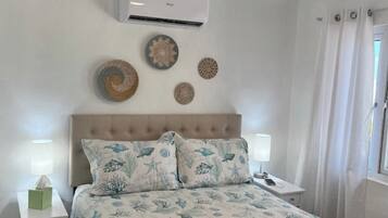 A bedroom with a bed, nightstands, an air conditioner, ceiling fan, and decorative plates on the wall.