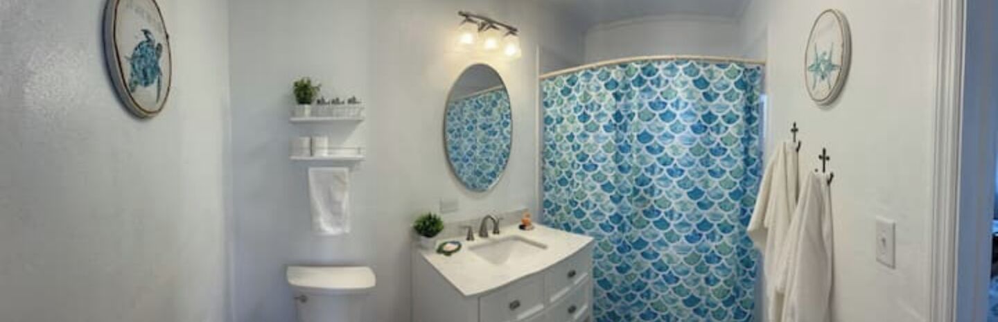 A bathroom with a white sink, mirror, and vanity, a blue patterned shower curtain, and a small shelf with toiletries.