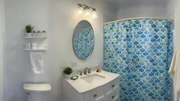 A bathroom with a white sink, mirror, and vanity, a blue patterned shower curtain, and a small shelf with toiletries.