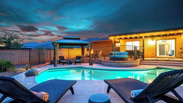 A poolside area with lounge chairs, a gazebo, and a building with a covered patio. - Desert Skies - Beautiful private Tucson home with great mountain views &  pool (Tucson)