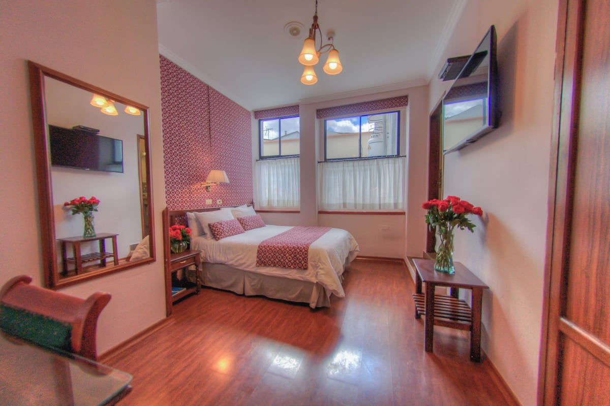 A neatly arranged bedroom with a bed, bedside tables, a mirror, and a TV mounted on the wall.
