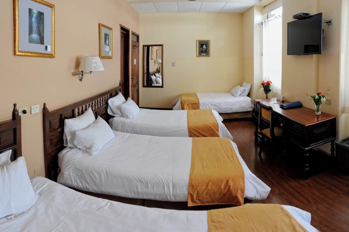 A hotel room with three beds, a desk, a television, and a window with curtains.