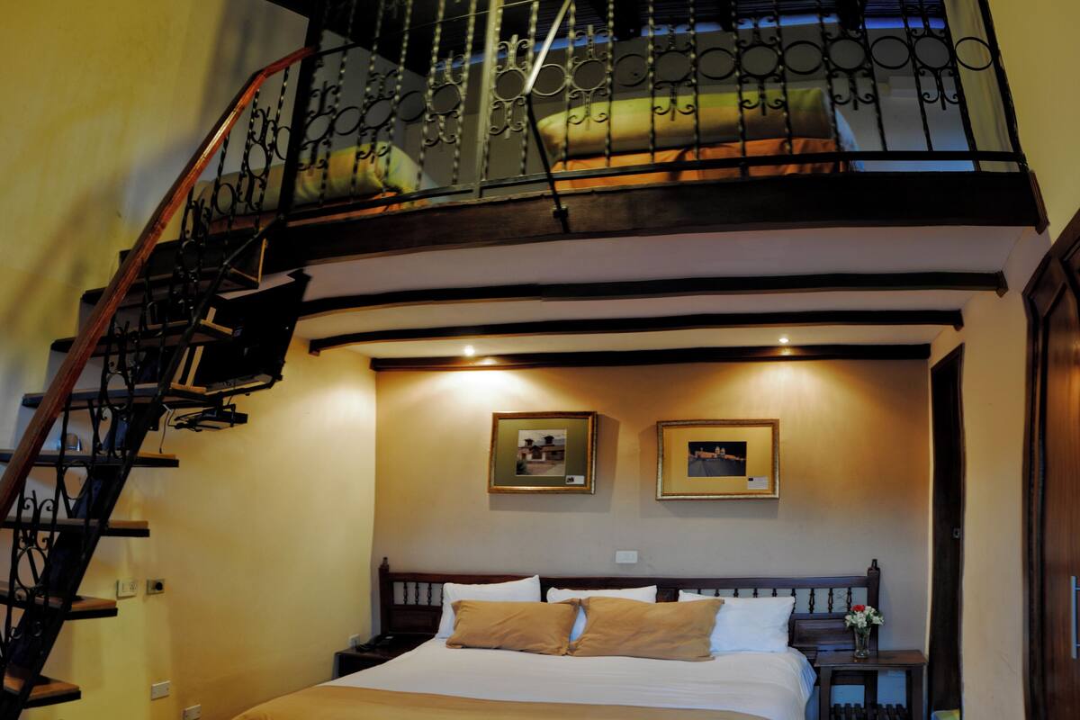 A bedroom with a large bed, a wooden staircase, and a balcony with a railing.