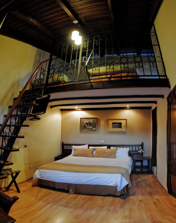 A bedroom with a large bed, a wooden staircase, and a balcony with a railing. - Real Audiencia Hotel (Quito)