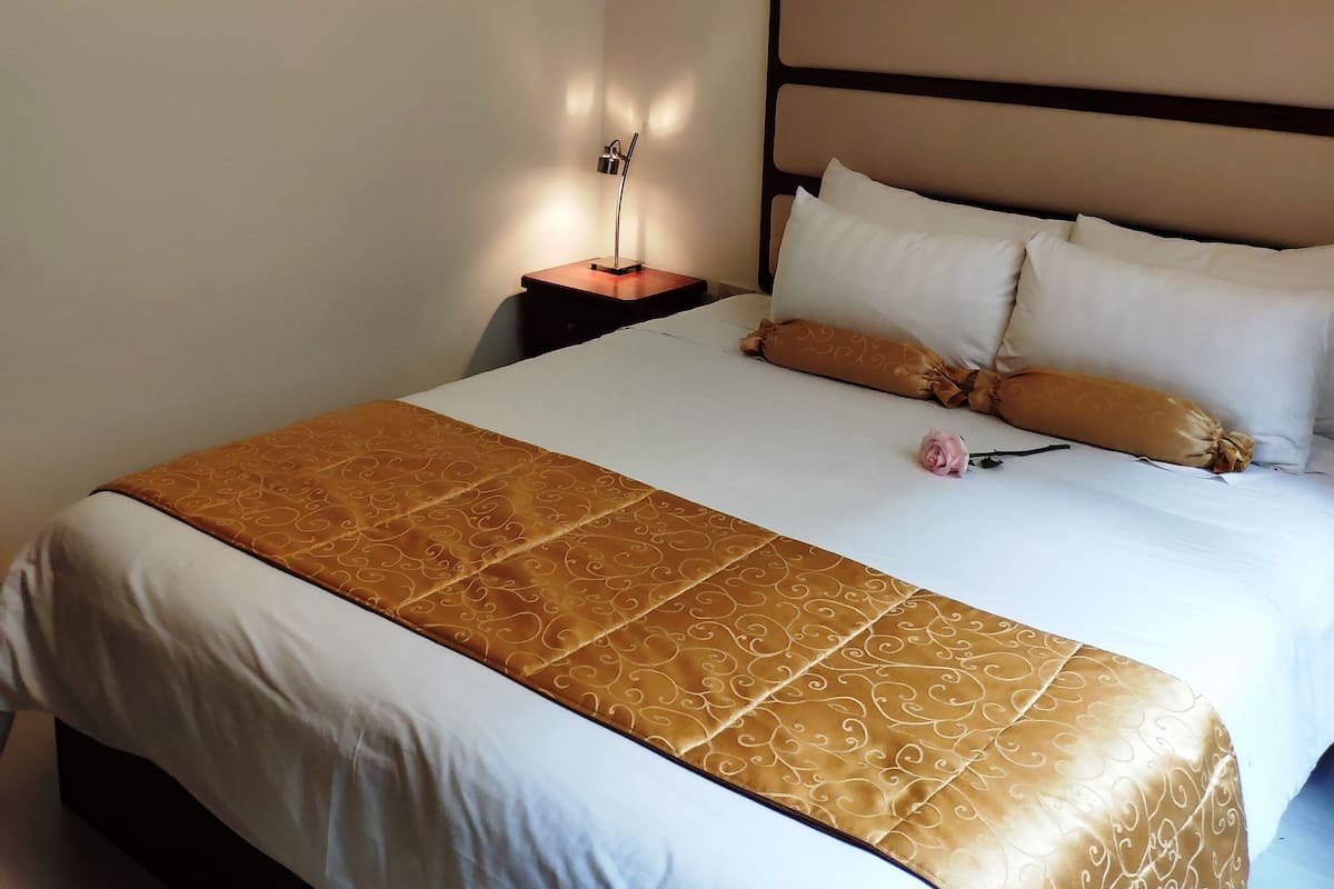 A neatly made bed with a patterned bedspread and pillows, a bedside lamp, and a framed picture on the wall.