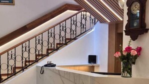 A modern interior with a marble reception desk, a wooden staircase with metal railings, and a wall-mounted clock. - Real Audiencia Hotel  (Quito)