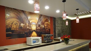 A reception area with a counter, a coffee machine, a vase with flowers, and a mural of an ornate interior. - Real Audiencia Hotel  (Quito)