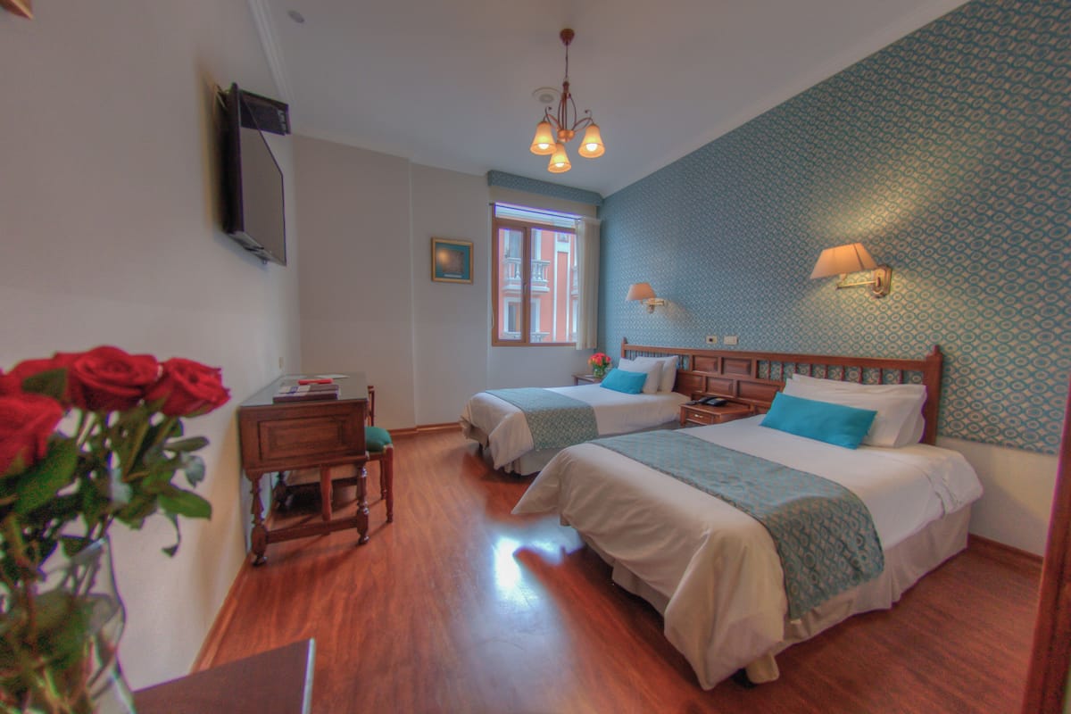 A hotel room with two beds, wooden furniture, a window, and a wall-mounted TV.