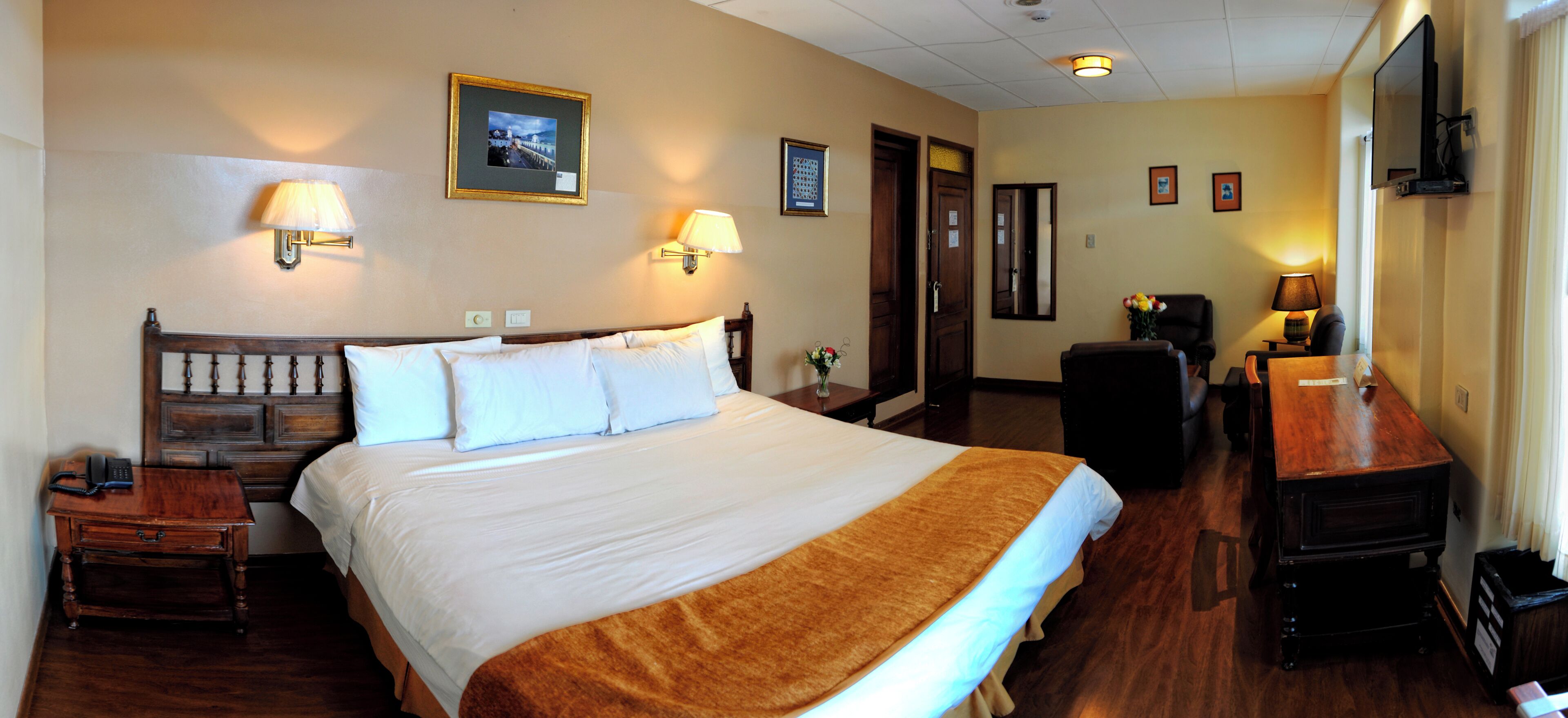Habitación de hotel con una cama grande, mesitas de noche, un escritorio, una silla y un televisor.