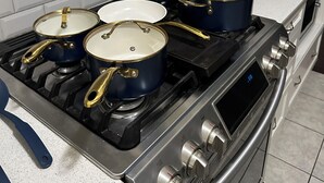 Een keuken met een gasfornuis, vier pannen en een digitaal bedieningspaneel.